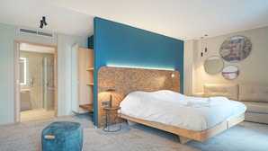 Une chambre à coucher moderne avec un lit, un pouf bleu, une petite table et un miroir fixé au mur.