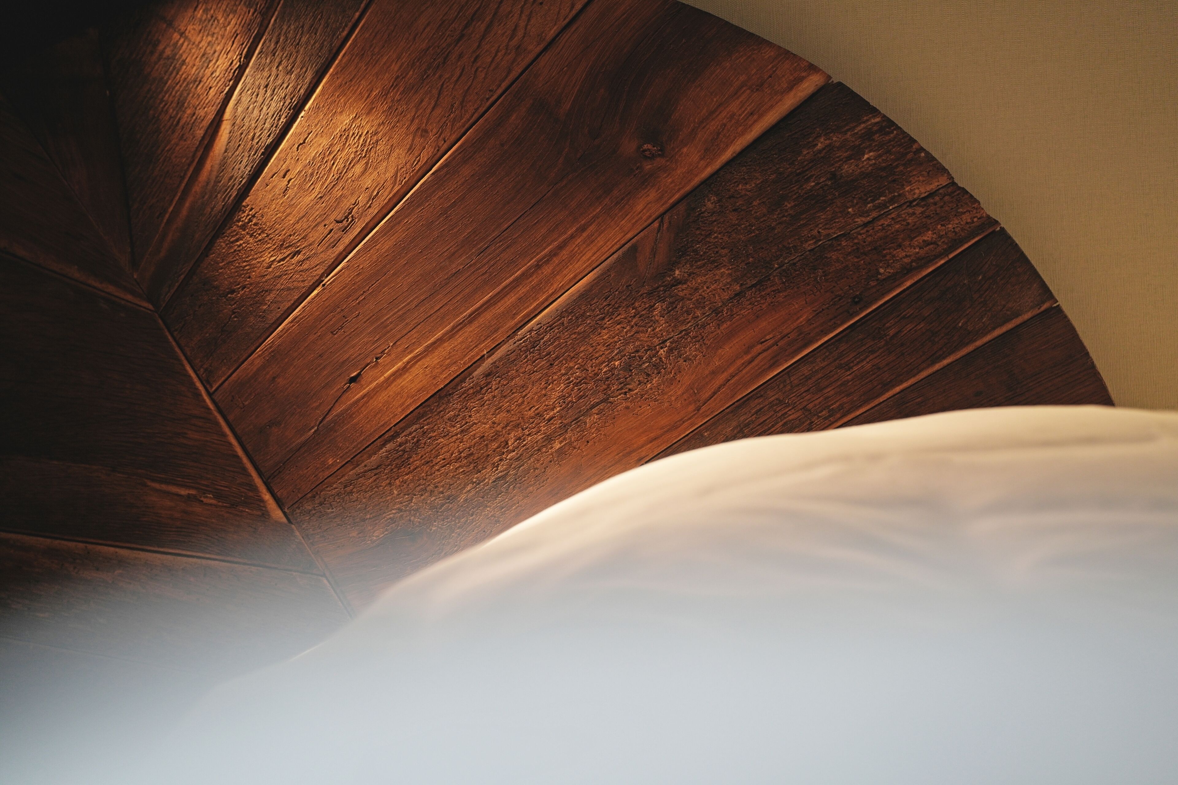 Techo de madera con diseño curvo, almohada blanca y una fuente de luz que genera un efecto luminoso.