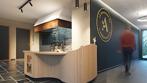 Un espace d’accueil moderne avec un comptoir en bois aux lignes courbes, un mur en pierre et un logo affiché sur le mur.