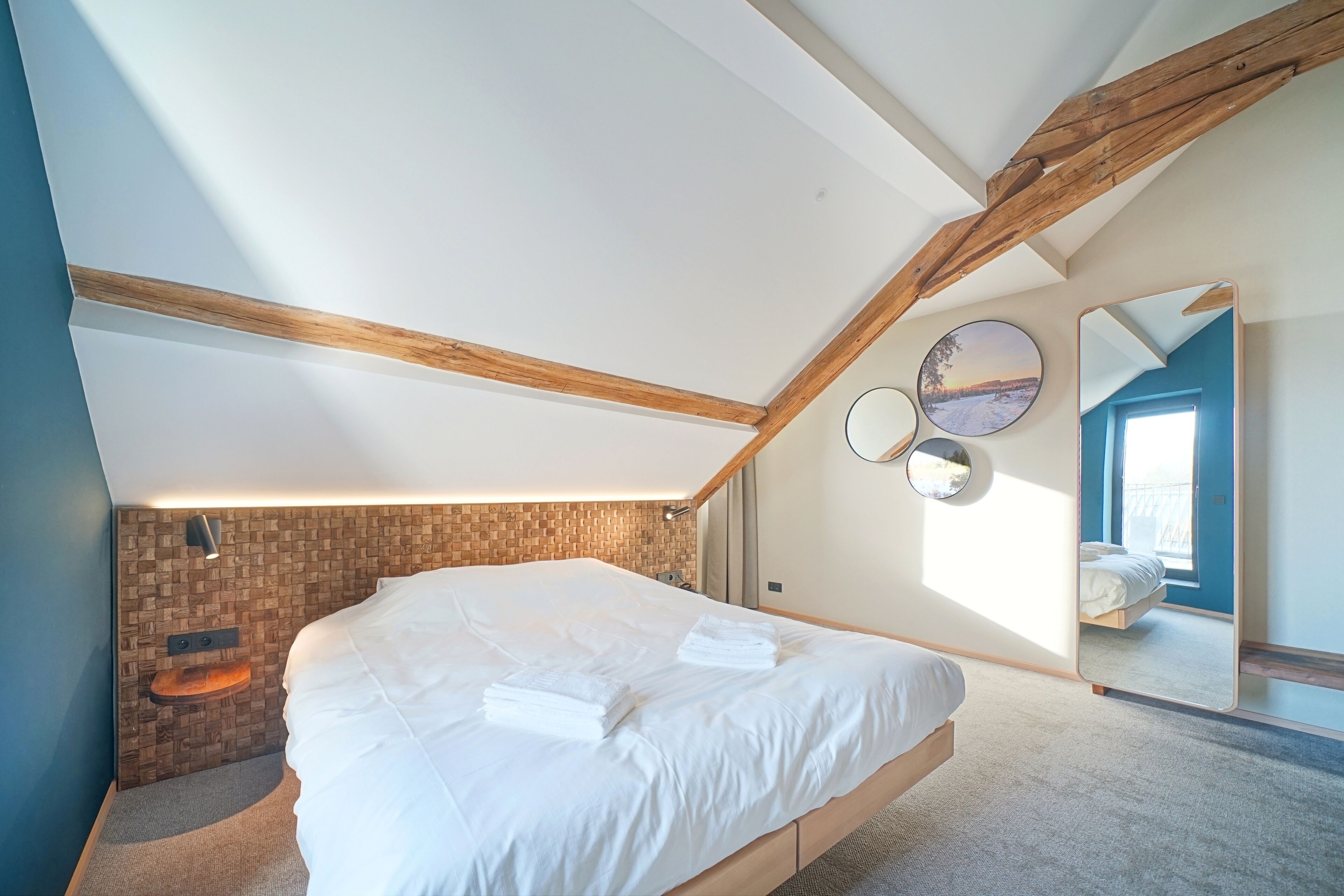 Une chambre moderne avec un lit en mezzanine, des poutres en bois, un mur d’accent en briques et un grand miroir.