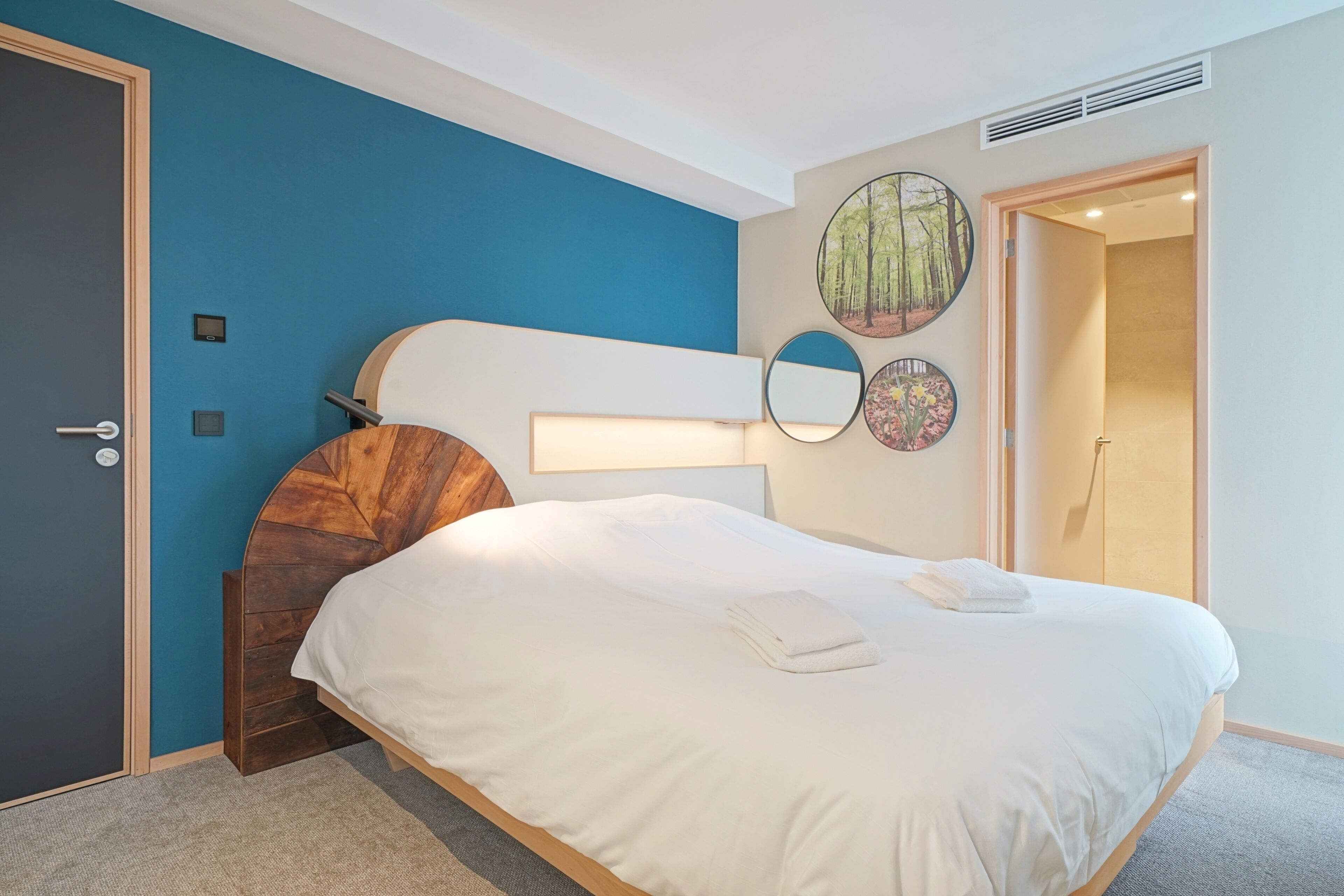A neatly made bed with white linens, a wooden headboard, and a wall-mounted lamp.