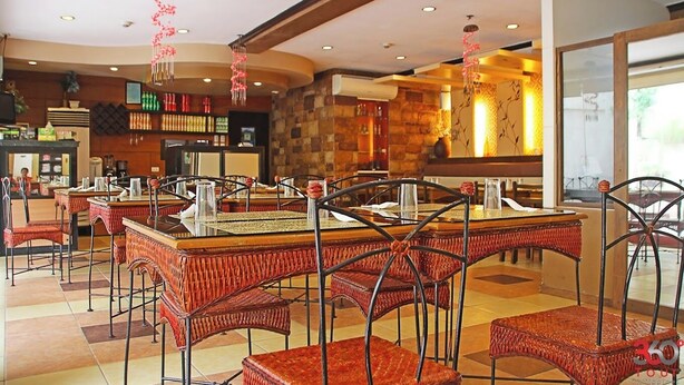 A restaurant with high tables and wicker chairs, a bar area, and a stone wall. - Hotel Palwa (Dumaguete)