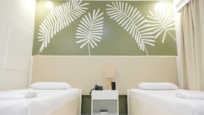 A hotel room with two beds, a nightstand with a lamp, and a wall with a leaf pattern. - Hotel Palwa (Dumaguete)