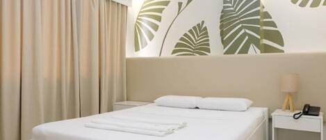 Habitación de hotel con cama, mesita de noche, lámpara y pared con diseño de hojas.
