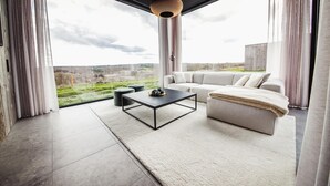 A modern living room with a large window, a black coffee table, a beige sofa, and a decorative light fixture. - Modern Maison Near Somme-leuze (Somme-Leuze)