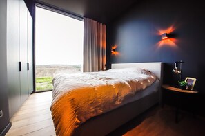 A modern bedroom with a large bed, a view through a sliding door, and a wall-mounted light fixture. - Modern Maison Near Somme-leuze (Somme-Leuze)