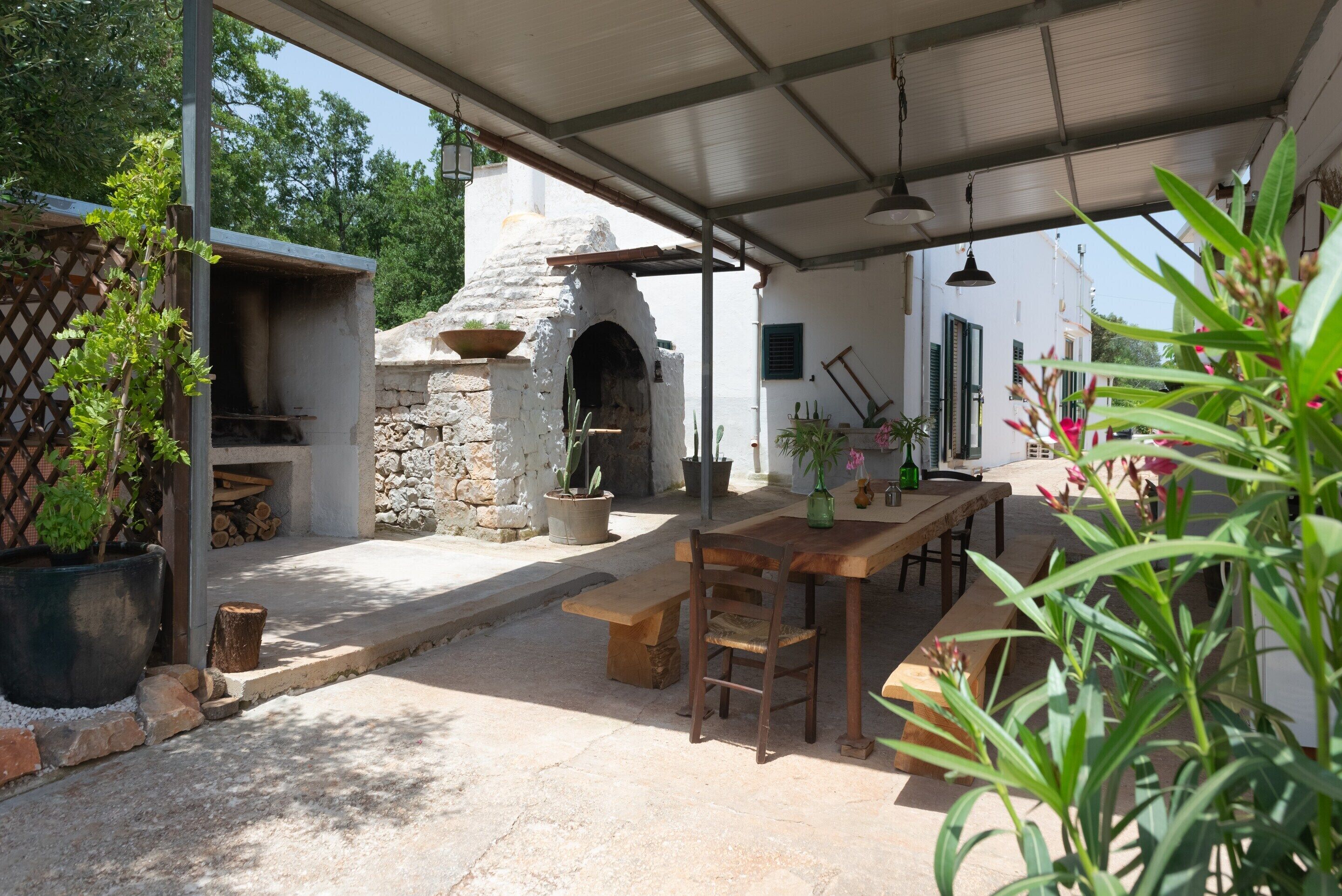 An outdoor patio with a stone oven, wooden table, and chairs.