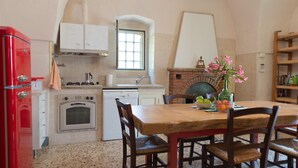 Una cocina con un refrigerador rojo, armarios blancos, un horno de ladrillo y una mesa de comedor de madera con sillas.