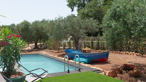 Una piscina con un bote, rodeada de olivos y un césped bien cuidado.