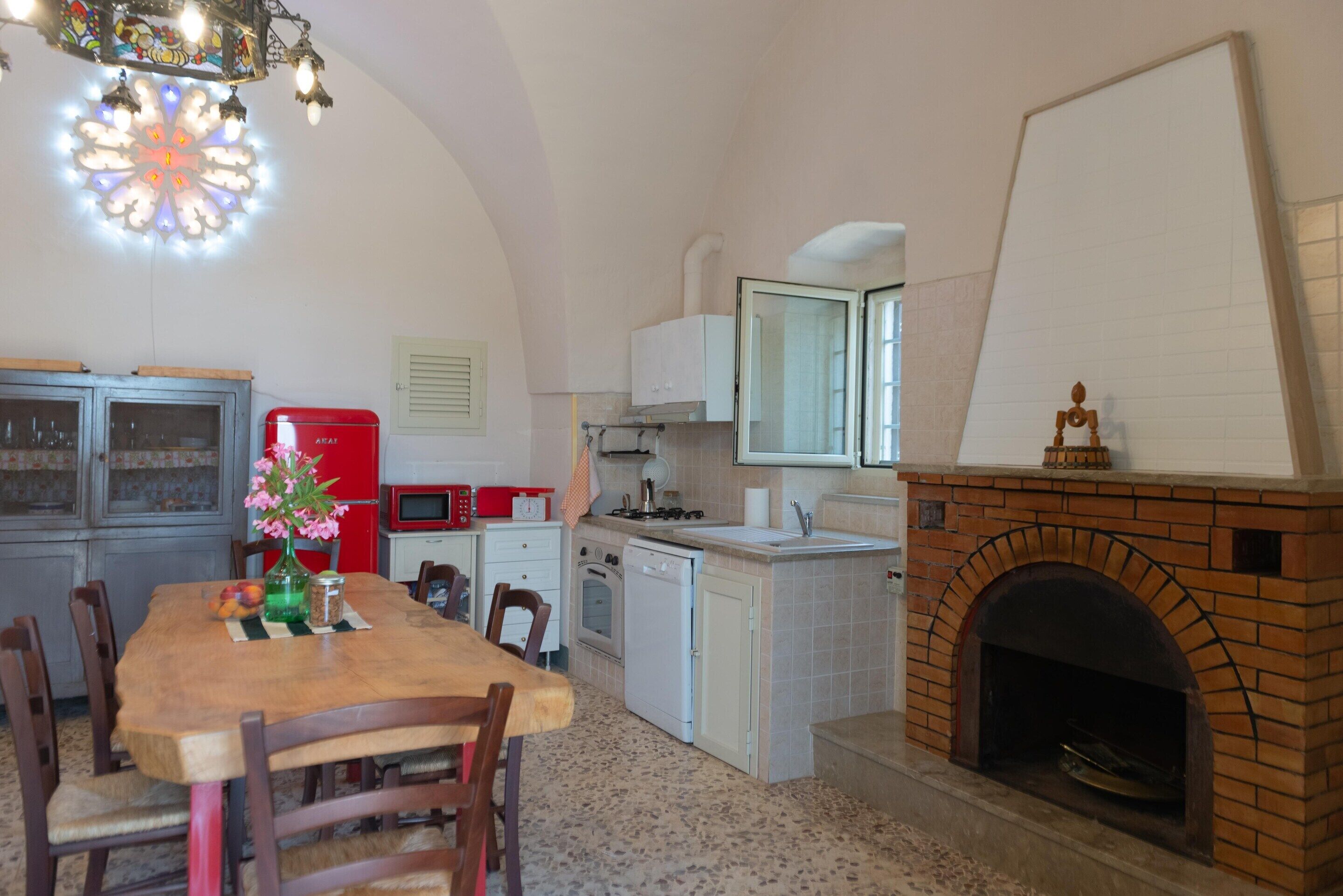 A compact kitchen with a dining table, chairs, a red refrigerator, a stove, and a brick fireplace.