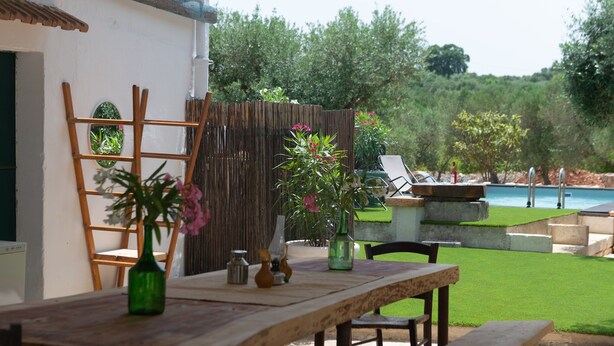 Un área de comedor al aire libre con una mesa y sillas de madera, y vistas a una piscina y follaje.