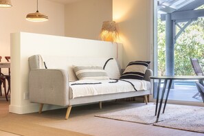 Een moderne woonkamer met een bank, een lamp en uitzicht door een glazen deur.