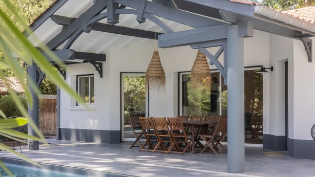 Un espace extérieur abrité, aménagé pour les repas, avec une piscine, des chaises en bois et des luminaires suspendus.