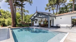Une piscine dotée d’une pergola, d’un espace salon extérieur et offrant une vue sur les arbres.