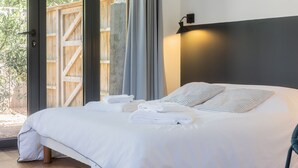 Un lit avec du linge de lit blanc et des oreillers à rayures, une porte en bois et un luminaire fixé au mur.