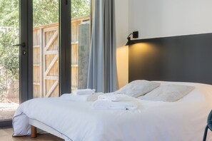 Een bed met witte lakens en gestreepte kussens, een houten deur en een wandlamp.