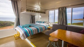 A bedroom with a bed, a sofa, a dining table, and a view of the sea. - Poolside Ocean View Pod (Marion Bay)
