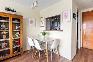 A dining area with a white table and chairs, a wooden cabinet with glass doors, and a kitchen visible through an open door.