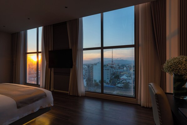 A hotel room with a large window, a bed, a TV, and a view of a cityscape. - Amana Boutique Hotel - Phan Thiet (Phu Thuy)