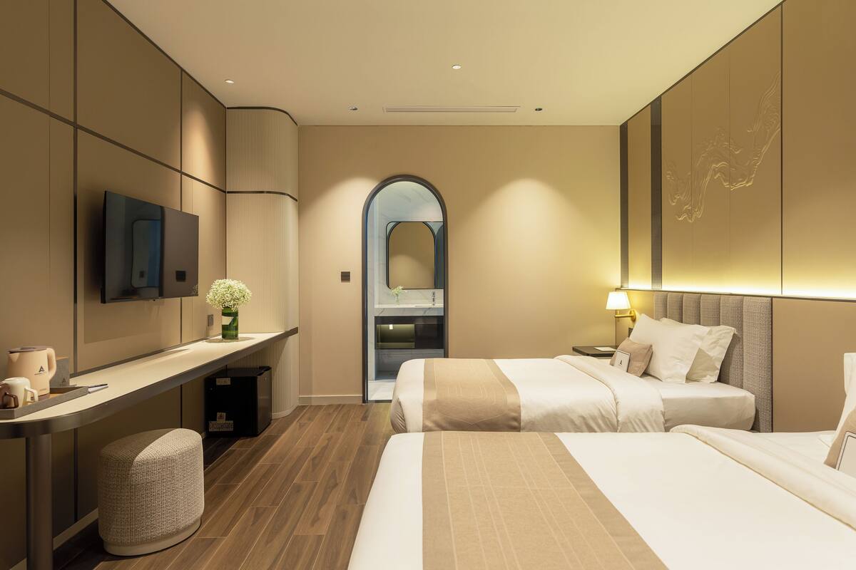 A modern hotel room with a bed, bedside table, and a desk with a chair.