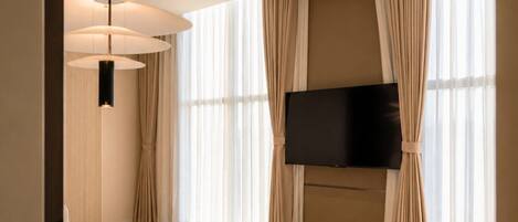 Un dormitorio moderno con una cama grande, un televisor de pantalla plana montado en la pared y un ventanal con cortinas.