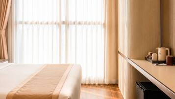 Habitación de hotel con dos camas, un escritorio y un ventanal con cortinas.