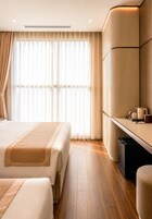 Habitación de hotel con dos camas, un escritorio y un ventanal con cortinas.