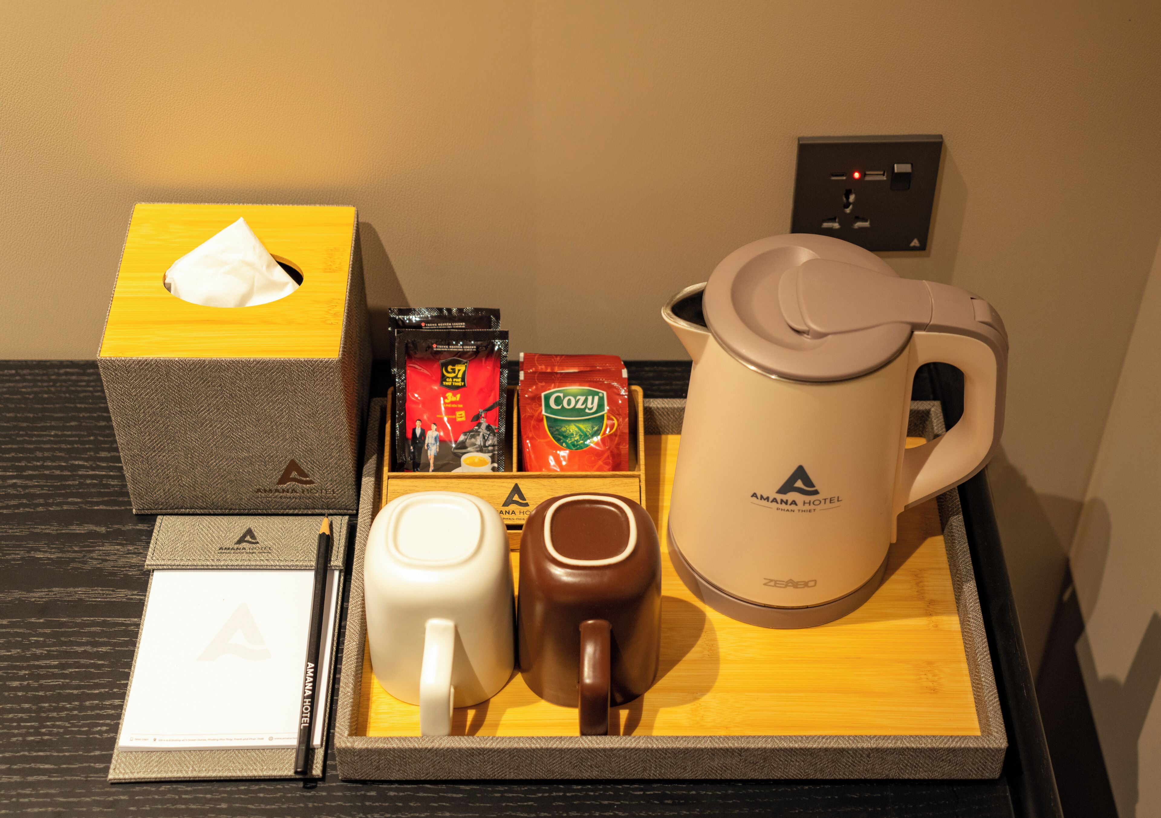 A tray with a tissue box, coffee packets, a coffee pot, a mug, and a notebook.