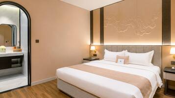 A hotel room with a large bed, bedside lamps, a mirror, and a wooden floor.