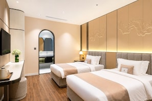 Camera d'albergo con due letti, una scrivania, uno specchio e un bagno parzialmente visibile attraverso un arco.