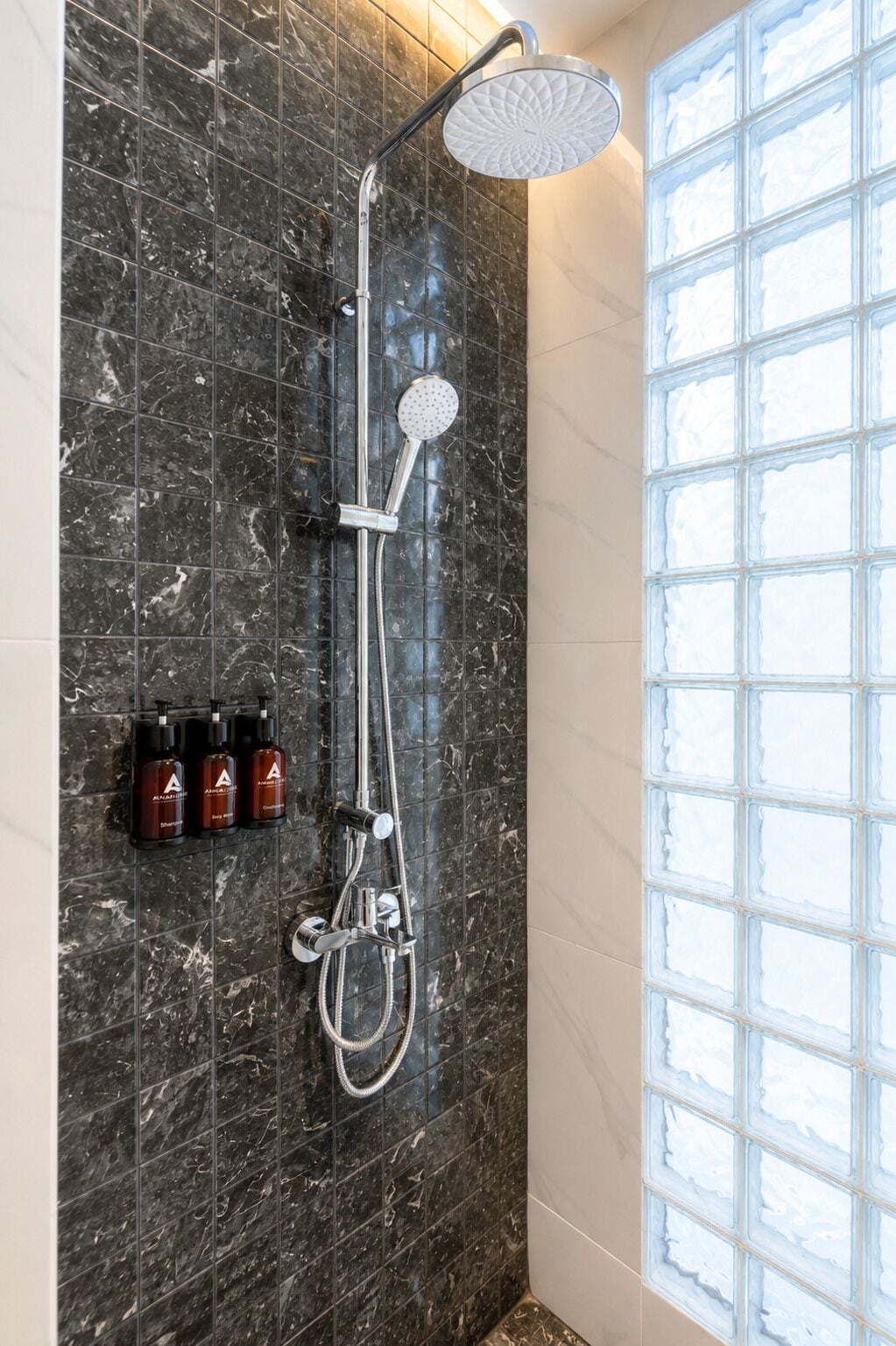 A modern bathroom with a shower, marble tiles, and a window with frosted glass.