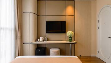 A modern hotel room with a bed, a bedside table, a TV, and a small stool.
