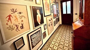 A hallway with a patterned floor, framed artwork on the walls, and a wooden cabinet.