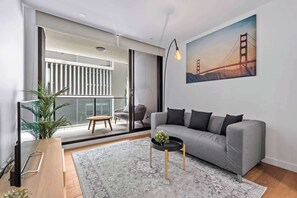 Una sala de estar moderna con un sofá gris, una mesa de centro, un ventanal grande y un cuadro de un puente.