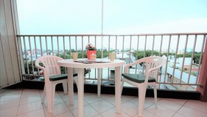 Ein Balkon mit rundem Tisch, zwei Stühlen, einem Blumentopf und Blick auf die Stadt.