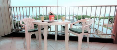 A balcony with a round table and two chairs, a potted plant, and a view of the cityscape.