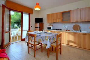 A kitchen with wooden cabinets, a dining table with chairs, a microwave, and a television.