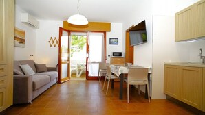 A compact living space with a sofa, dining table, chairs, a kitchen area with cabinets, a microwave, and a television.