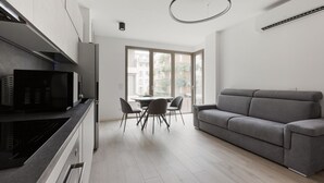 A modern kitchen with a dining area, a grey sofa, and a large window.