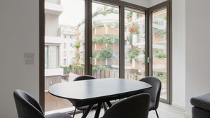 A modern apartment with a dining area, large sliding glass doors, and a view of neighboring buildings.