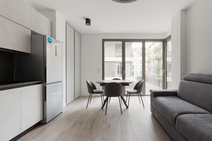A modern kitchen with a built-in refrigerator, a dining area with a table and chairs, and a grey sofa.