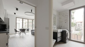 A modern kitchen with a built-in oven, a dining area with a table and chairs, and a large window with a view of buildings.