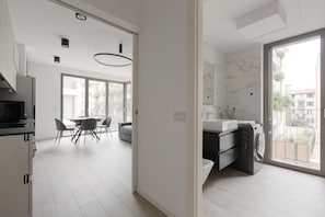 A modern kitchen with a built-in oven, a dining area with a table and chairs, and a large window with a view of buildings.