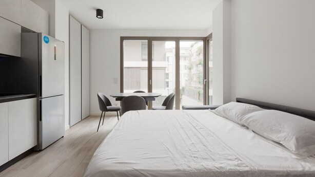 A modern bedroom with a large bed, a desk, and a refrigerator.