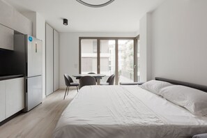 A modern bedroom with a large bed, a desk, and a refrigerator.