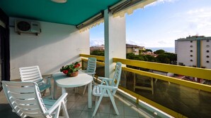 A balcony with a table and chairs, a potted plant, and a view of the sea and buildings. - Apartment with sea view terrace (Bibione)