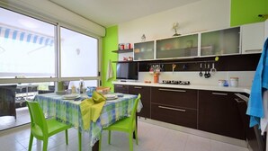 A compact kitchen with a dining area, featuring a table with chairs, a window, and a view of the outside. - Flat in Bibione with terrace (Bibione)