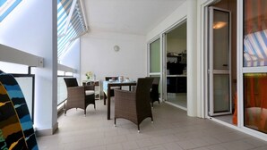 A spacious room with a dining area, wicker chairs, a table, and a sliding glass door leading to a kitchen. - Flat in Bibione with terrace (Bibione)