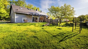 A house with a sloped roof, a covered porch, and a fenced yard with a swing set. - Vacation home Bimmelbahn track 2 (Olbersdorf)