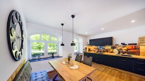 A modern kitchen with a wooden dining table, pendant lights, and a large clock on the wall. - Vacation home Bimmelbahn track 2 (Olbersdorf)